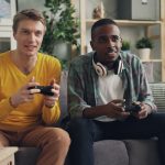 Two men sitting on a couch playing video games, focused and engaged. — Play on a Direct Baccarat Website That Combines Glamou